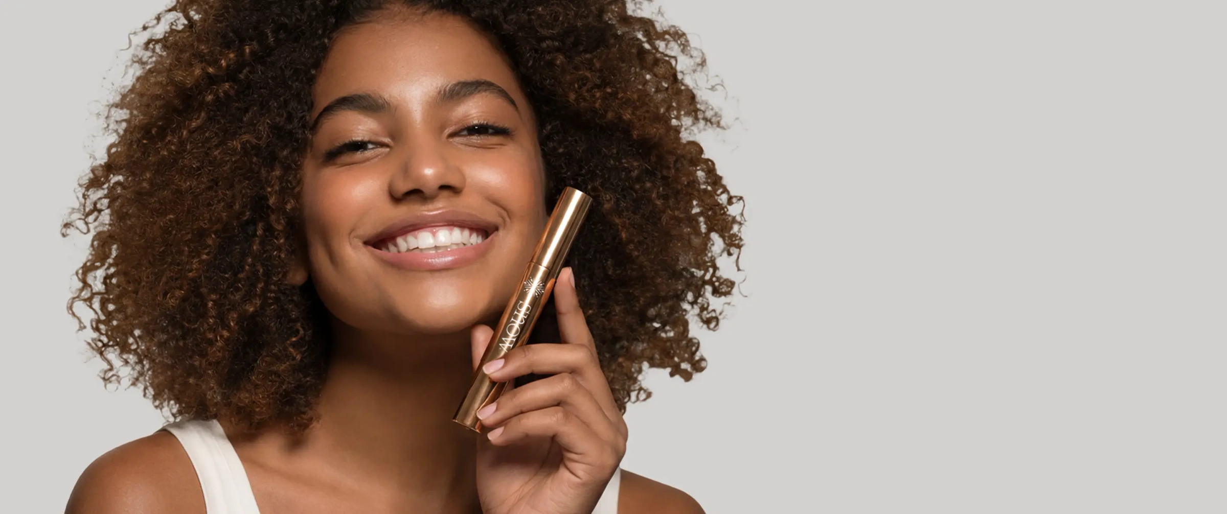 A smiling woman with curly hair holding a Snow whitening pen to her cheek