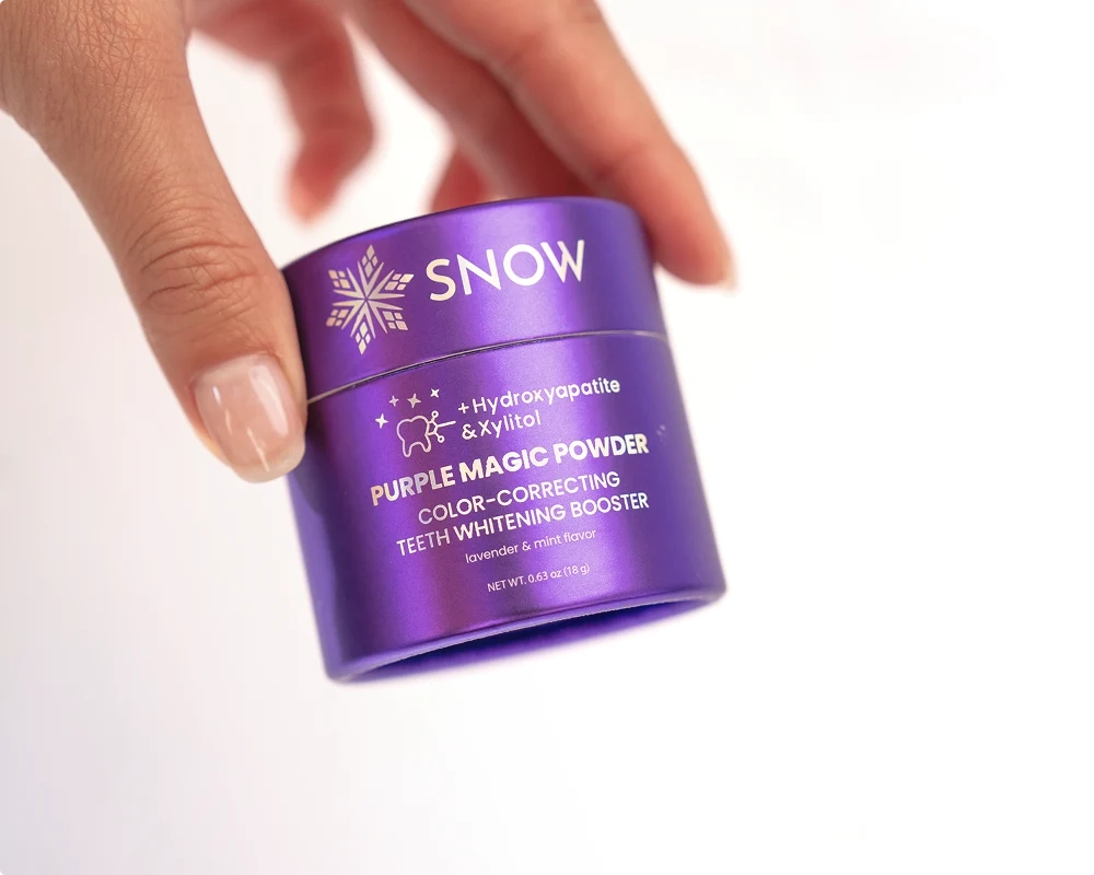 A hand tilting the Snow Purple Magic Powder jar